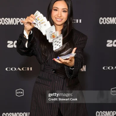 Anna DeGuzman performing a card flourish on a branded step-and-repeat backdrop