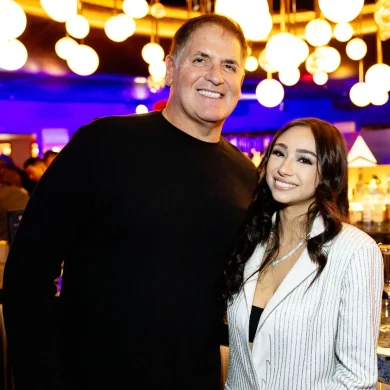 Anna DeGuzman posing with Mark Cuban under warm pendant lights at a venue event